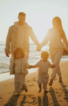 a family walking on the beach holding hands and smiling at the camera with the sun shining behind them