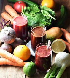 there are many fruits and vegetables on the table with juices in glasses next to each other