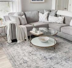 a living room with gray couches, white pillows and a rug on the floor