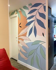 a room with a painted wall in the shape of leaves and plants, next to a red couch