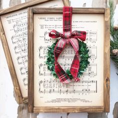 two framed christmas wreaths with red and green plaid ribbon hanging on sheet music sheets