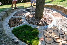 two people standing next to a tree in a yard with rocks and grass on the ground