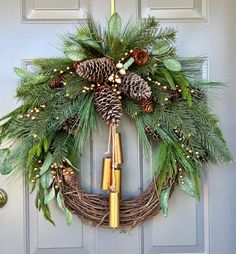 a wreath with pine cones and evergreens hanging from the front door, decorated with gold bells