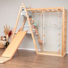 a child climbing on a slide in a play room with wooden flooring and white walls