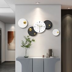 a white and black clock mounted to the side of a wall next to a plant