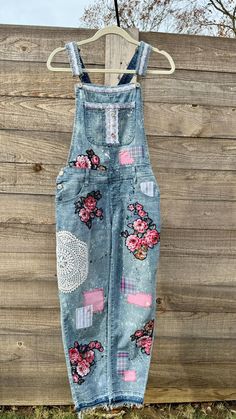 an old pair of denim overalls hanging on a wooden fence with flowers and lace