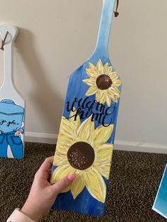 a hand holding up a painted wooden sign with sunflowers on it