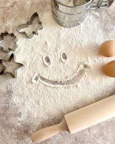 a smiley face made out of flour next to two cookie cutters and an egg