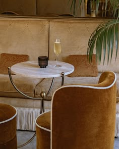 two chairs and a table in front of a couch with a wine glass on it