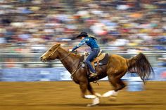 a man riding on the back of a brown horse in front of a large crowd