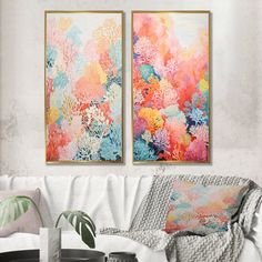 two paintings hanging on the wall above a white couch in a living room with a coffee table