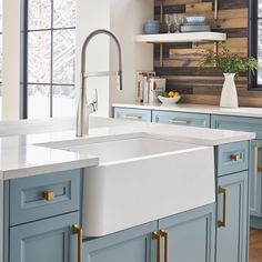 a kitchen with blue cabinets, white counter tops and gold pulls on the faucet