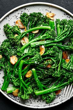 a white plate topped with broccoli covered in nuts and green vegetables next to a fork