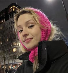 a woman wearing a pink knitted hat and scarf in front of a building at night