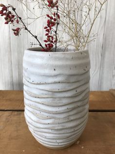 a white vase with red flowers in it on a wooden table next to a wall