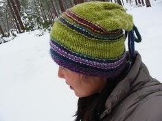 a woman wearing a green hat while standing in the snow with trees behind her on a snowy day