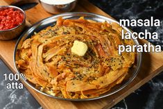 a pan filled with food sitting on top of a wooden cutting board next to a bowl of sauce