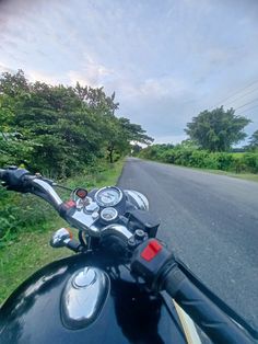 a motorcycle is parked on the side of the road near some grass and trees in the background