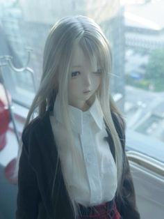 a doll with long blonde hair standing in front of a window