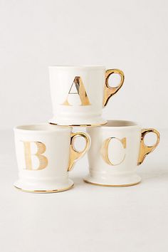 four white coffee cups with gold letters on them and the words anthropologie alphabet mug