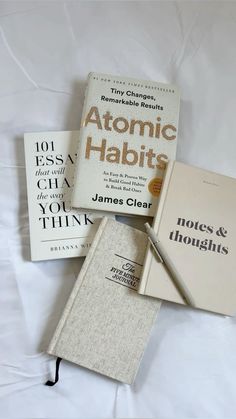 three books sitting on top of each other next to a pen and book bag with the title atomic habitts written in it