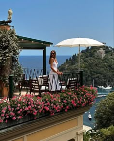 a woman standing on top of a balcony next to flowers and an umbrella in front of the ocean