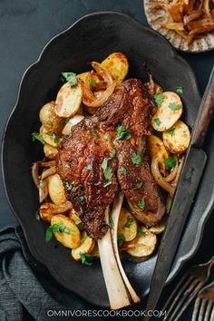 steak with potatoes and parsley in a skillet on a black plate next to silverware