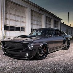 a black car parked in front of a building with garage doors on the other side