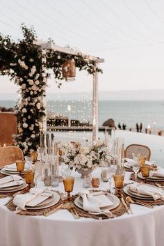 a table set with plates and place settings for an outdoor dinner by the ocean at sunset