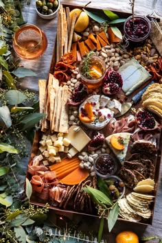 an assortment of cheeses, crackers and fruit on a wooden table surrounded by greenery