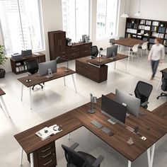 an office with desks and chairs in the middle of it, two people walking by