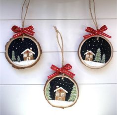 three christmas ornaments hanging on the wall with red bows and snow covered houses in the background