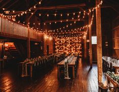 the inside of a barn with tables and lights strung from the ceiling, along with wooden flooring