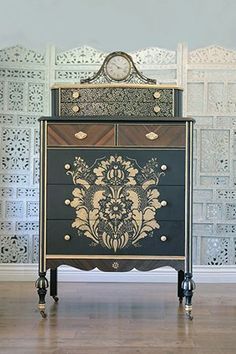 an ornate chest of drawers in front of a wallpapered room with a clock on top