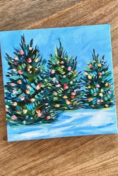 an acrylic painting of three pine trees in the snow on a wooden surface