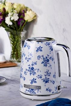 a blue and white flowered tea kettle on a marble countertop with flowers in the background