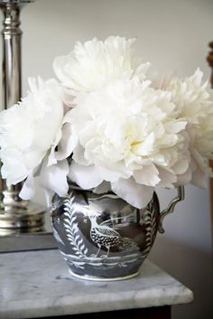 a vase with white flowers in it sitting on a marble table next to a mirror