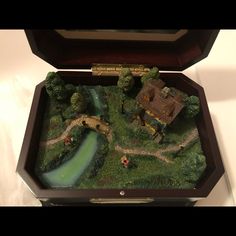 an open box with a miniature house and bridge in it