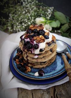 a stack of pancakes topped with blueberries and whipped cream on a plate next to flowers