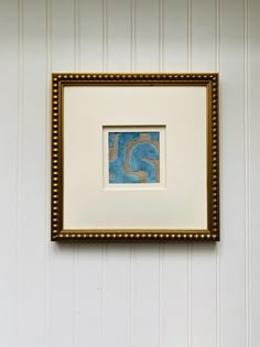 a white wall with a blue and gold frame hanging on it's side next to a toilet