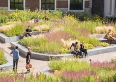 several people sitting on benches in the middle of a garden with flowers and plants around them