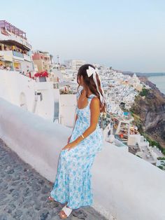 a woman in a blue and white dress is standing on a ledge looking at the ocean