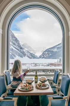 a woman sitting at a table with two plates of food in front of an open window