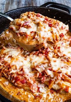 a skillet filled with lasagna sauce and cheese being spooned into the casserole