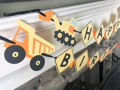 a birthday banner with construction vehicles hanging from it's sides in front of a fireplace