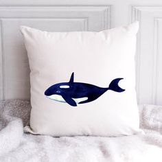 a pillow with an orca on it sitting on a white blanket next to a wall