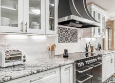 a kitchen with white cabinets and marble counter tops, along with an open range hood over the stove