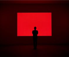 a person standing in front of a large red square on a dark room with no people