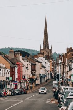 an old town street with cars parked on both sides and a steeple in the background