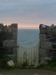 an open gate with the ocean in the back ground and sky above it at sunset